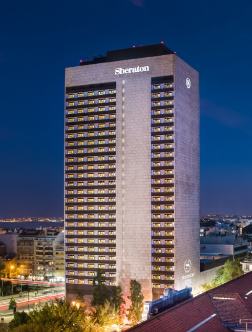 Illuminated facade of the Sheraton hotel at night, with a city view in the background