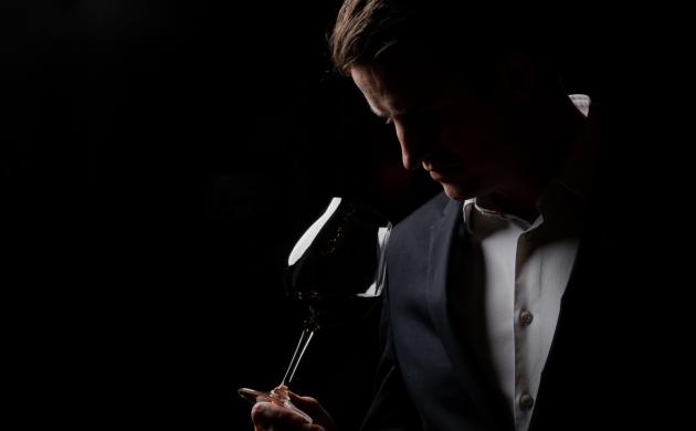 Elegant man in suit holding a glass of red wine in low light, sensory tasting experience for father’s day celebration in Lisbon