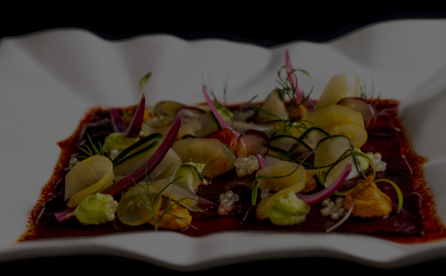 A colorful gourmet dish presented on a white plate, featuring thin slices of marinated vegetables and creamy textures on a beetroot base.